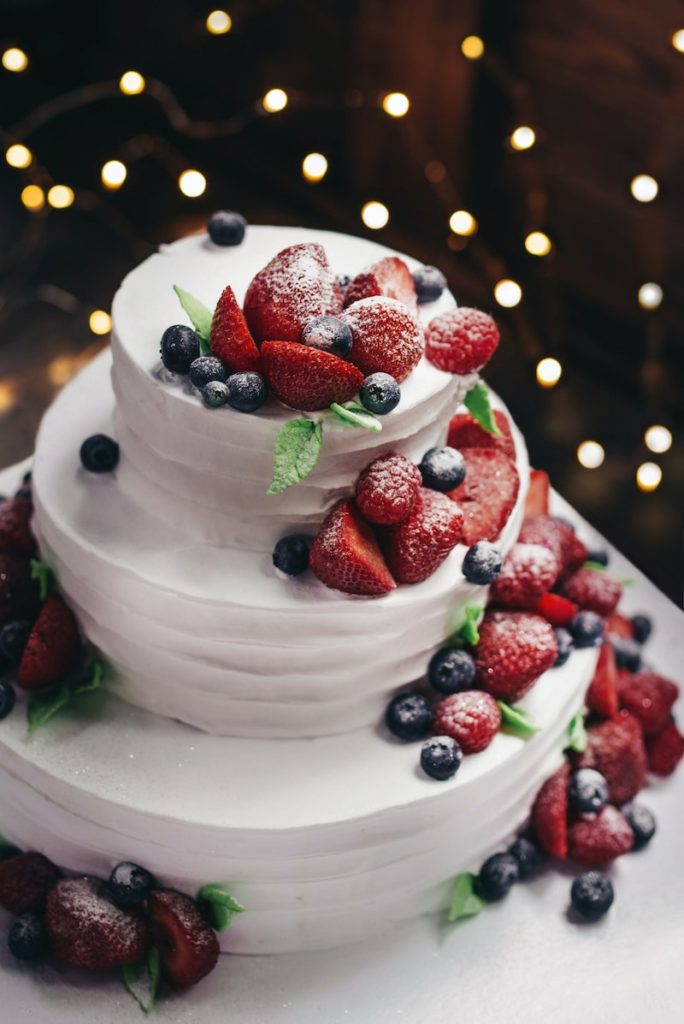 Wedding cake with red white and blue theme strawberries and blueberries atop white frosting