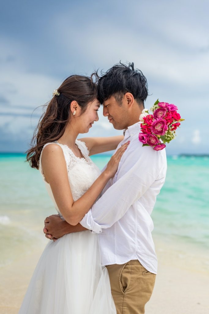 Couple embracing on their wedding day on a beach with pink flowers